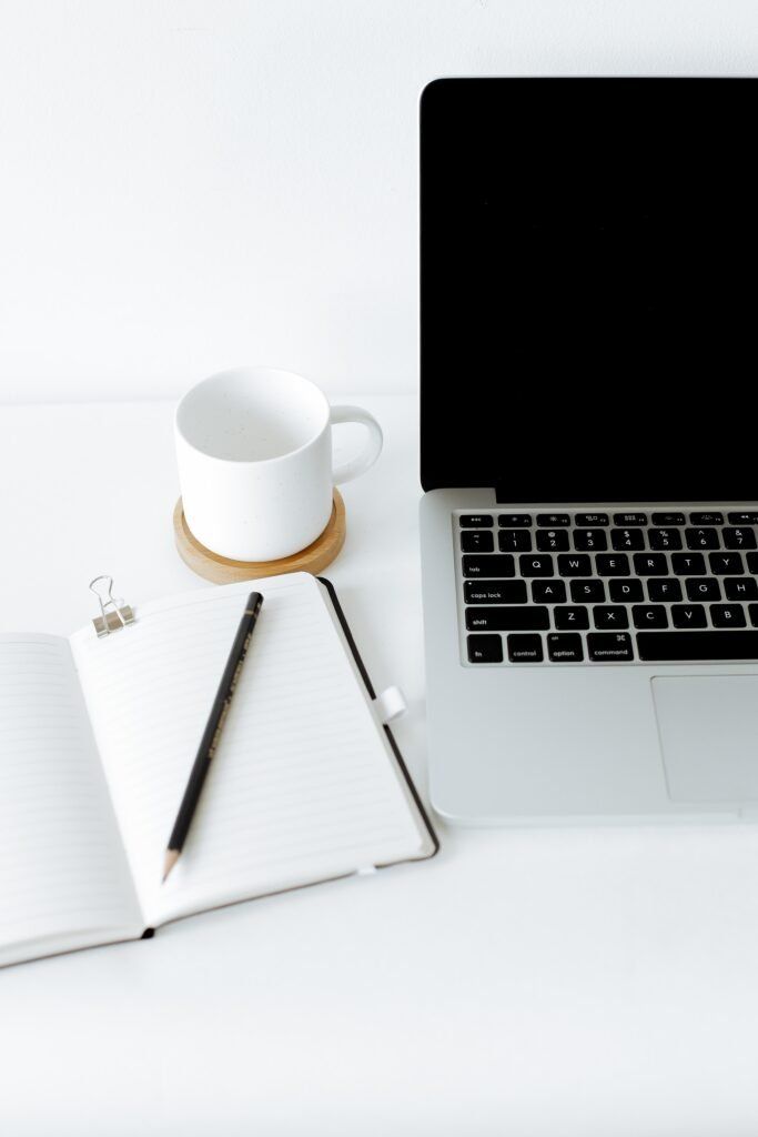 Bild eines Laptops, einer Tasse Kaffee und einem Notizbuch mit Stift